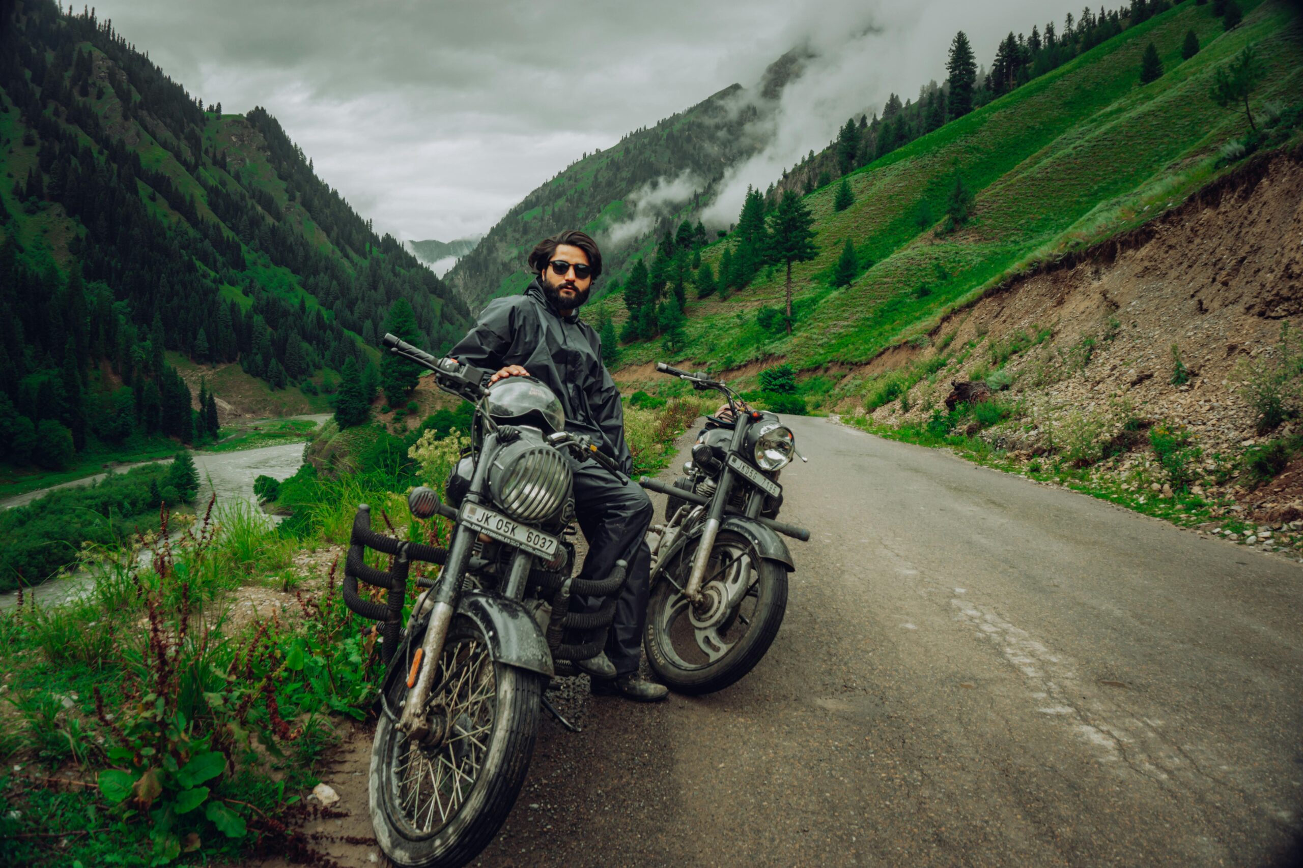 A motorcyclist pauses on a winding road in the lush Gurez Valley, surrounded by mountains.